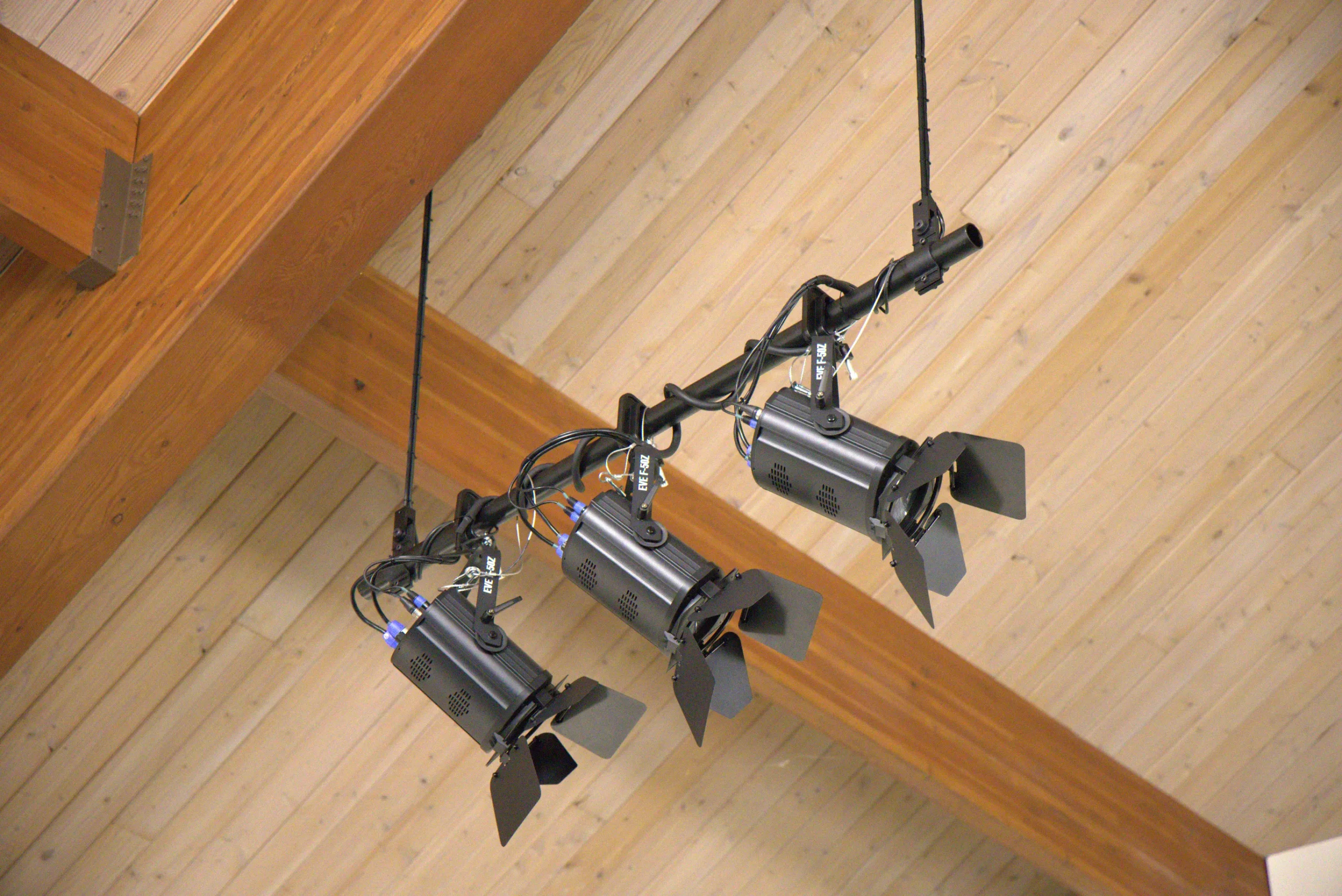 Three Chauvet stage lighting fixtures mounted from a wood sanctuary ceiling